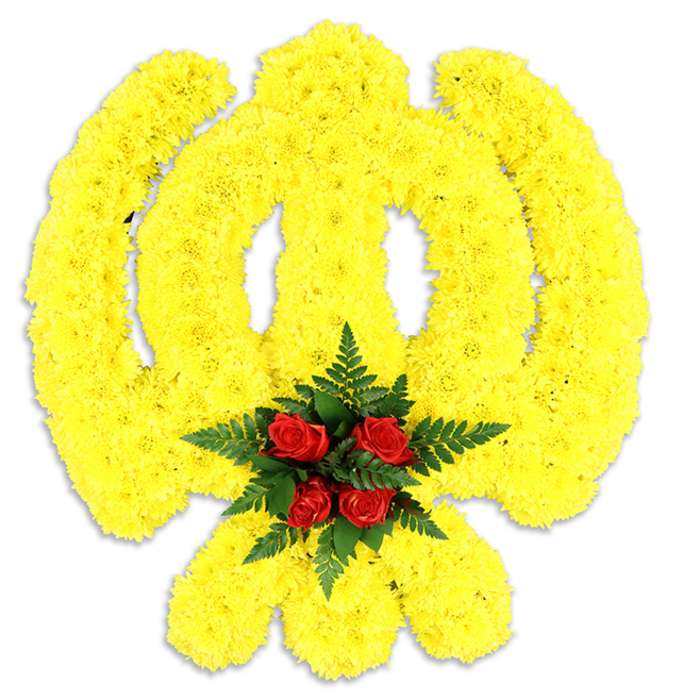 Dominating the visual field is a large, ceremonial Khanda formed from countless bright yellow chrysanthemum blooms, arranged so densely that the emblem reads as a continuous, plush surface against a pure white backdrop. The florist's hand is visible in the way each curve and point of the symbol - the circular chakkar, the two crossing kirpans and the central double-edged khanda - has been sculpted by aligning floral heads to create smooth lines and a slightly three-dimensional profile. At the core of the design sits a grouped handful of deep red roses, five or six tight buds whose lush, velvety petals stand in high relief against the surrounding yellow; these are cradled by swathes of dark green fern fronds that spill outward, introducing a cool, feathery texture and framing the heart. The composition rests on a white surface that casts a soft, neutral shadow beneath the piece, indicating a freestanding tribute commonly used at funerals, memorial services or cultural commemorations. The colours read with instant clarity: the sunny yellow communicates warmth and remembrance, the red roses signal respect and lasting affection, and the green foliage offers an understated sense of renewal. Having created memorial displays for Sikh families and community events across Bracknell and surrounding parishes, I recognise how this arrangement balances religious symbolism and floral technique to provide a comforting, dignified presence whether displayed in a local gurdwara or brought to a family service.