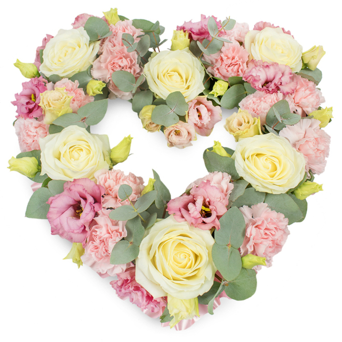 A luxuriously full, heart-shaped funeral wreath sits against a pure white background, every inch of its surface brimming with pastel blooms and soothing greenery. The heart is formed with meticulous symmetry, its curves defined by clusters of large cream and pale yellow roses, their tightly layered, velvety petals spiralling inward to form elegant, full heads that serve as the anchors of the design. Between and around these roses, a generous scattering of light pink carnations fills the spaces, their frilled petals adding a feather-soft texture and enhancing the romantic, gentle mood. Richer mauve and deep pink lisianthus blossoms are spaced thoughtfully throughout, some with slightly open, cupped petals revealing darker centres, giving the wreath a subtle depth and a touch of sophistication without overpowering the overall softness. Threaded through the flowers are sprigs of silvery-green eucalyptus, their round, matte leaves providing a cool contrast to the warm pastels and lending a quiet, natural structure to the arrangement. Tiny yellow-green buds, still tightly closed, peek out from between the petals, suggesting freshness and the enduring cycle of life. The wreath appears dense and plush, with no bare spaces, creating an impression of abundance and heartfelt care. It carries an atmosphere of peace, remembrance, and gentle farewell, the kind of tribute that might rest beside a photograph at a memorial service or accompany a casket at a funeral in Bracknell's local chapels. Crafted with the sensitivity of an experienced Bracknell florist, this heart-shaped arrangement feels like a final embrace, reflecting the love of family and friends gathering to honour a life lived with meaning.