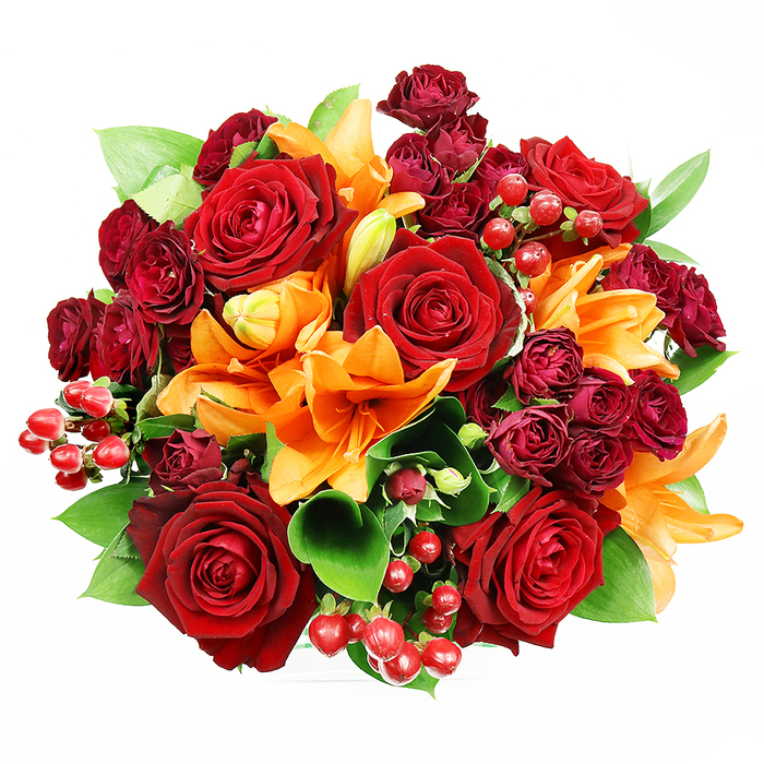 Captured straight above on a clean white plane, this abundant floral composition reads like a classic narrative of love and celebration told in red, orange, and green. Several large, deep red roses dominate the view, their smooth, velvety petals layered into rich spirals that suggest both romance and tradition. Interspersed are bright orange Asiatic lilies with trumpet-shaped petals-some fully splayed to reveal their stigmas and stamens, others in elegant, tapering buds-adding structural contrast and a lively, uplifting note. Small, tightly bunched burgundy spray roses provide textured clusters that deepen the palette and create subtle shadow and depth among the larger blooms. Glossy red hypericum berries appear in neat clusters, their round, reflective surfaces giving the bouquet a festive, tactile punctuation. Broad, glossy green leaves, reminiscent of ruscus or salal, slip between flowers to give volume, breathing room, and a verdant backdrop that sharpens the warm tones. The lighting is gentle and even, illuminating petal surfaces and the delicate veins of leaves without harsh shadows, so each element reads clearly. This arrangement feels equally suited to an intimate anniversary, an autumn celebration, or a thoughtful gift to brighten a home near South Hill Park or the riverside walks of Bracknell Forest. The composition's scent-soft rose sweetness undercut by the lily's spicy-citrus tang-completes the sensory picture of a bouquet meant to comfort, delight, and mark a memorable moment.